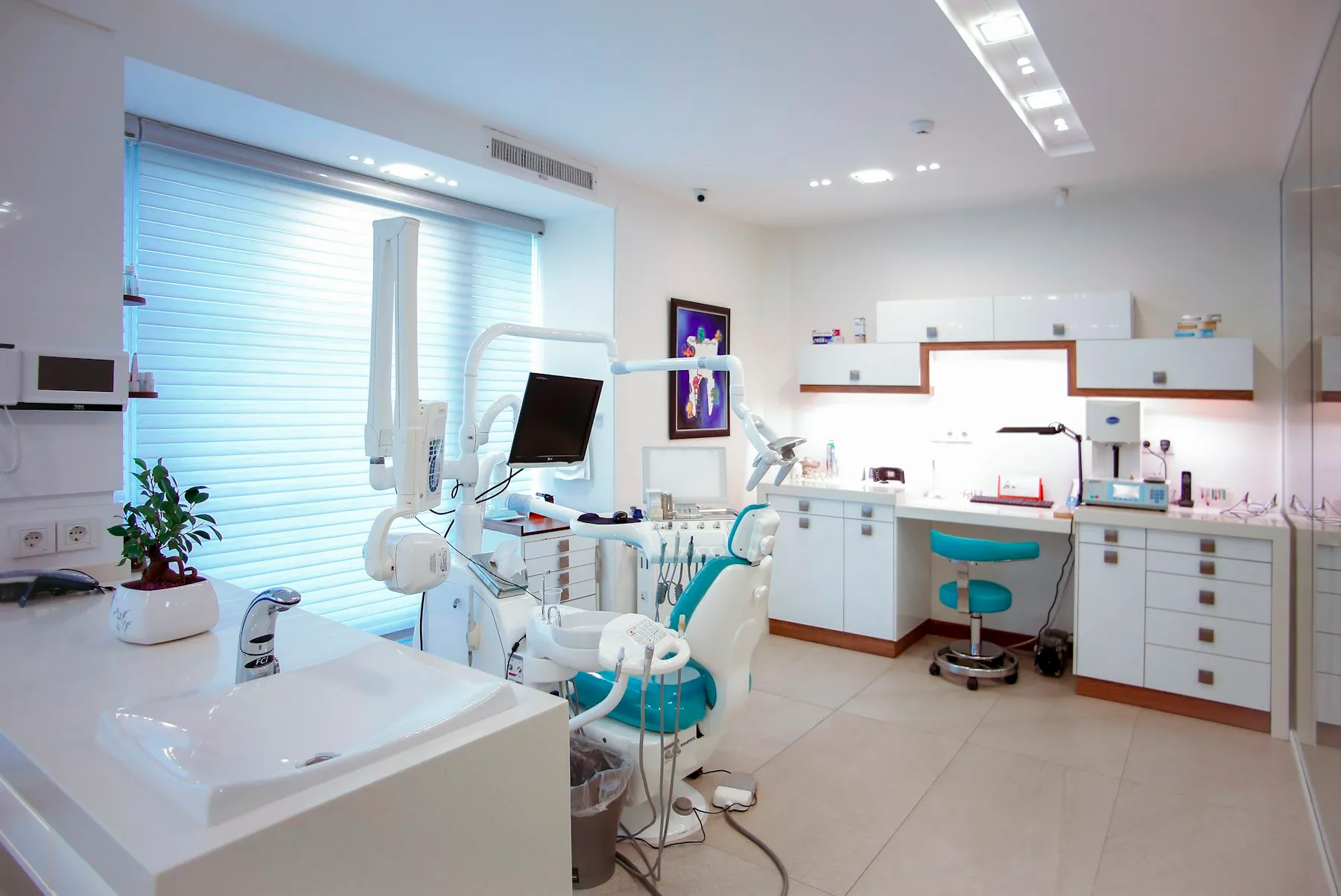 Cabinetul stomatologic: fotoliu dentar, lavoar și dulapuri albe, cu lumină de la fereastră
